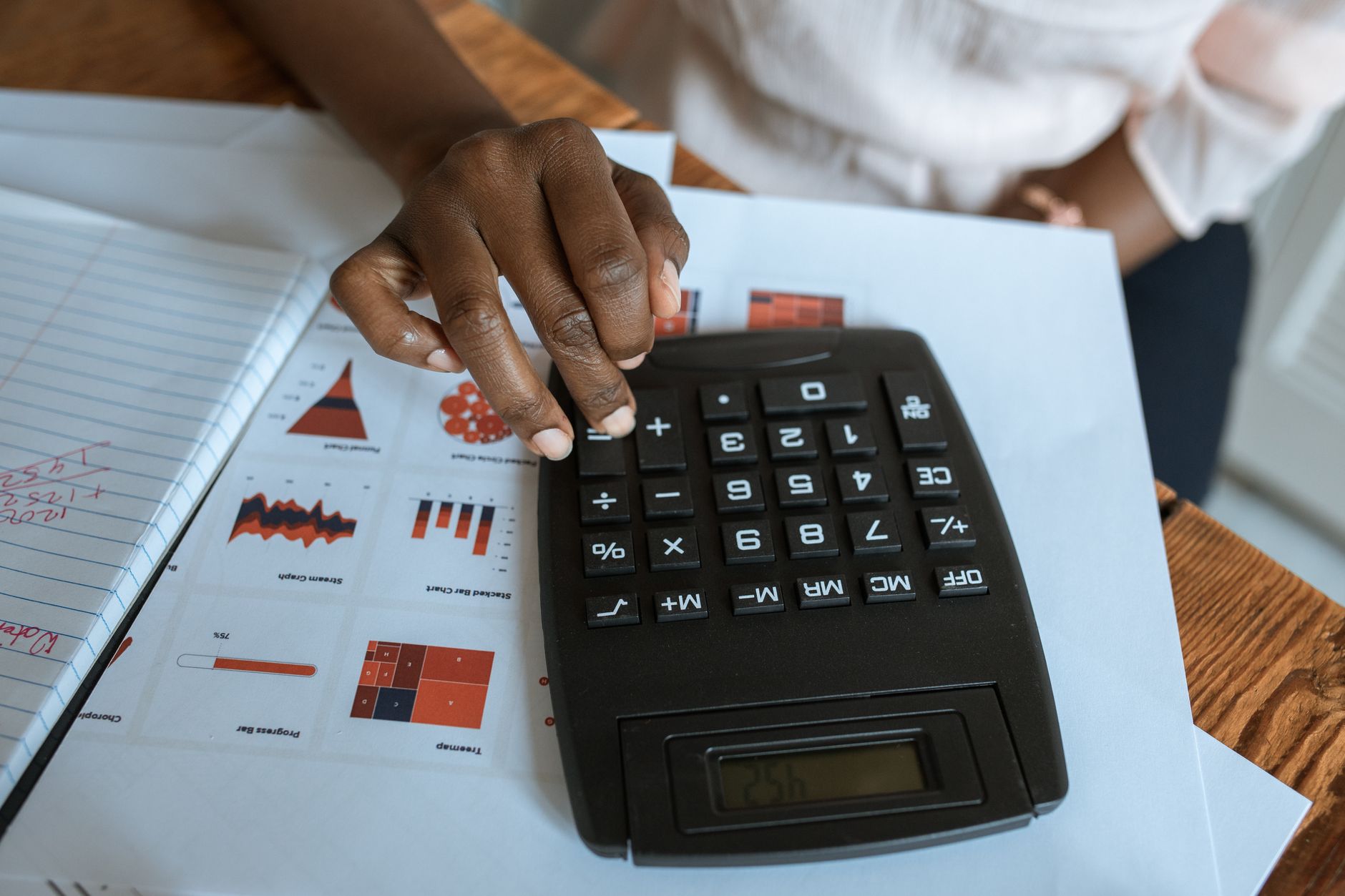 Une main posée sur une calculatrice de bureau à côté de documents affichant divers graphiques.